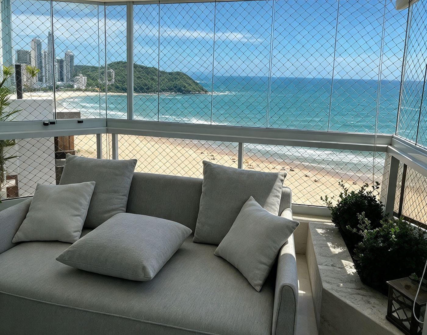 Sacada envidraçada com rede de proteção e sofá, vista para a praia e a orla de Balneário Camboriú