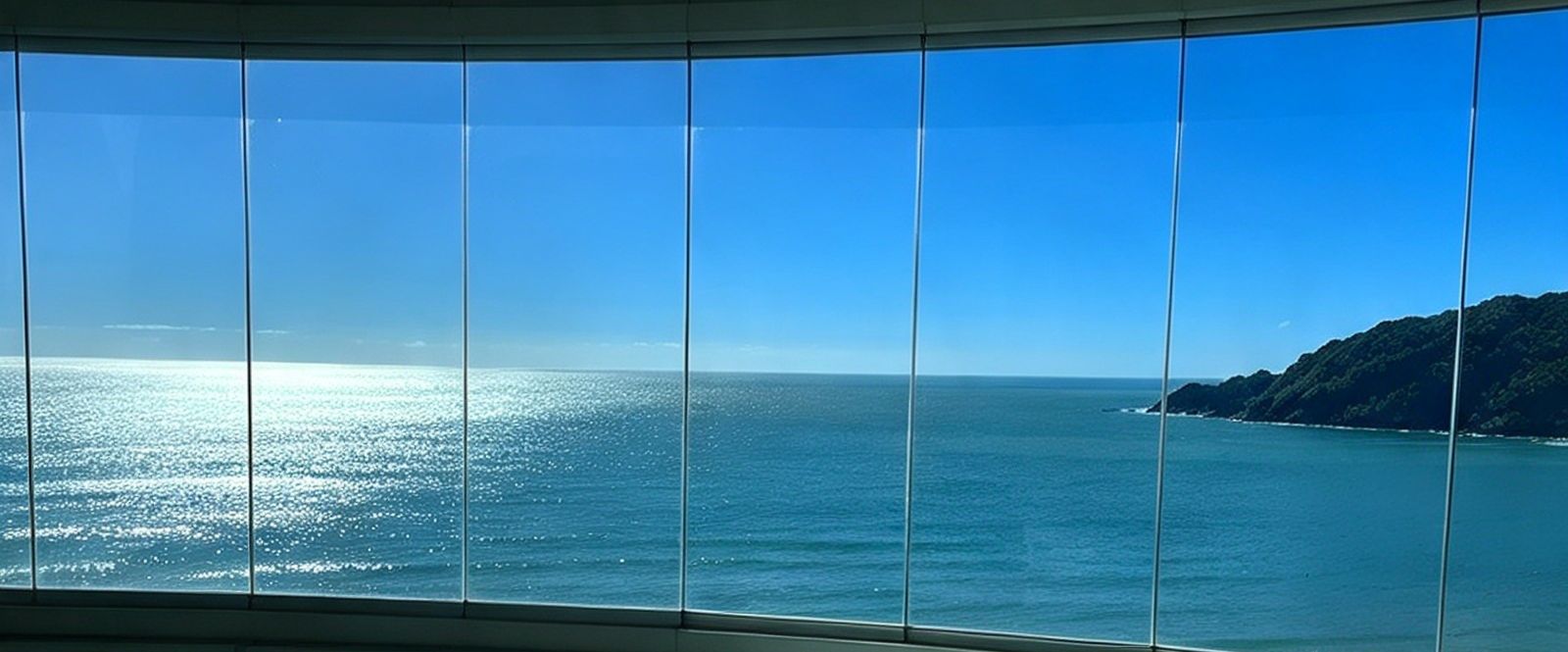 Fechamento de sacada em curva com folhas de vidro alinhadas e vista para o mar